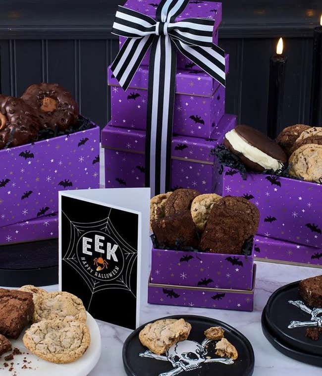 Purple gift box with black and white striped bow. On serving trays are mini candy corn bundt cakes and whoopie pies, chocolate brownies, and chocolate cookies