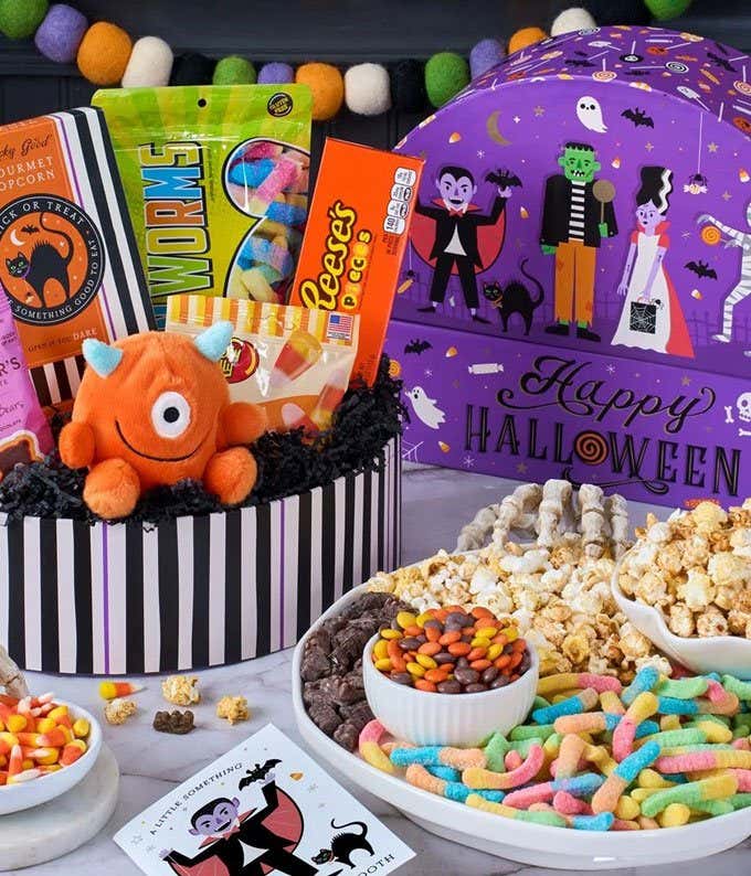 A gift box with a bag of dark chocolate cubetti, black & white cookies, halloween crispy rice treat. bag of candy corn, bag of gummy worms, and a Tony's Chocolonely Bar. 