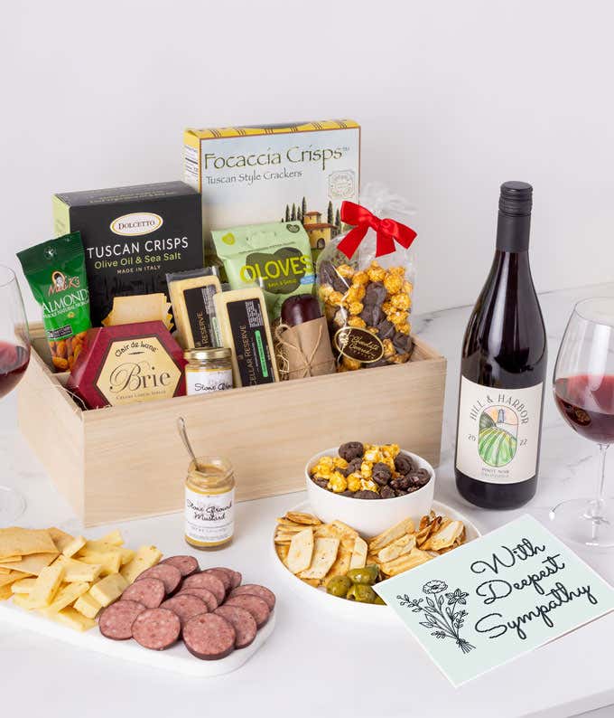 An abundent charcuterie gift set with Tuscan crisps, focaccia crackers, 3 cheeses, olives, mustard, summer sausag, almonds, chocolate-covered popcorn, a bottle of Pinot Noir, and a sympathy card. 