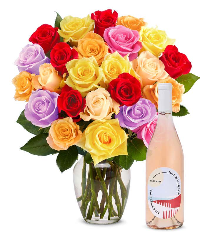 An exquisite bouquet of roses in a kaleidoscope of colors—vivid reds, soft pinks, warm oranges, sunny yellows, and gentle purples—arranged in a clear glass vase, accompanied by a sleek bottle of rose wine from California, 2023, embodying grace and festivi