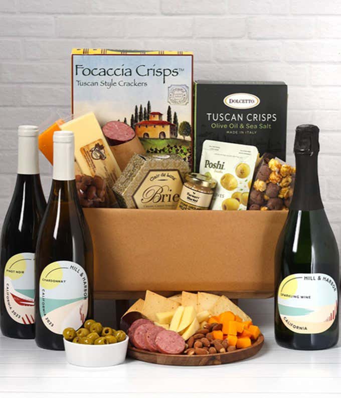 A wine and cheese gift set featuring bottles of Hill & Harbor Sparkling wine, Chardonnay, and Pinot Noir. Includes a variety of cheeses, crackers, olives, smoked almonds, summer sausage, and condiments.