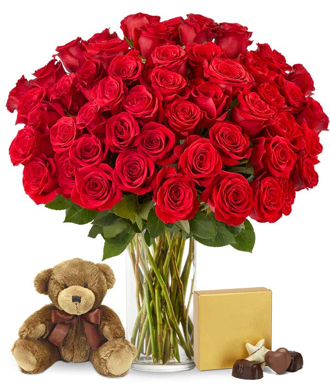 Image of 50 long-stemmed red roses in a tall cylinder vase, accompanied by a box of chocolates and a cuddly teddy bear, the perfect gift for expressing love and affection.