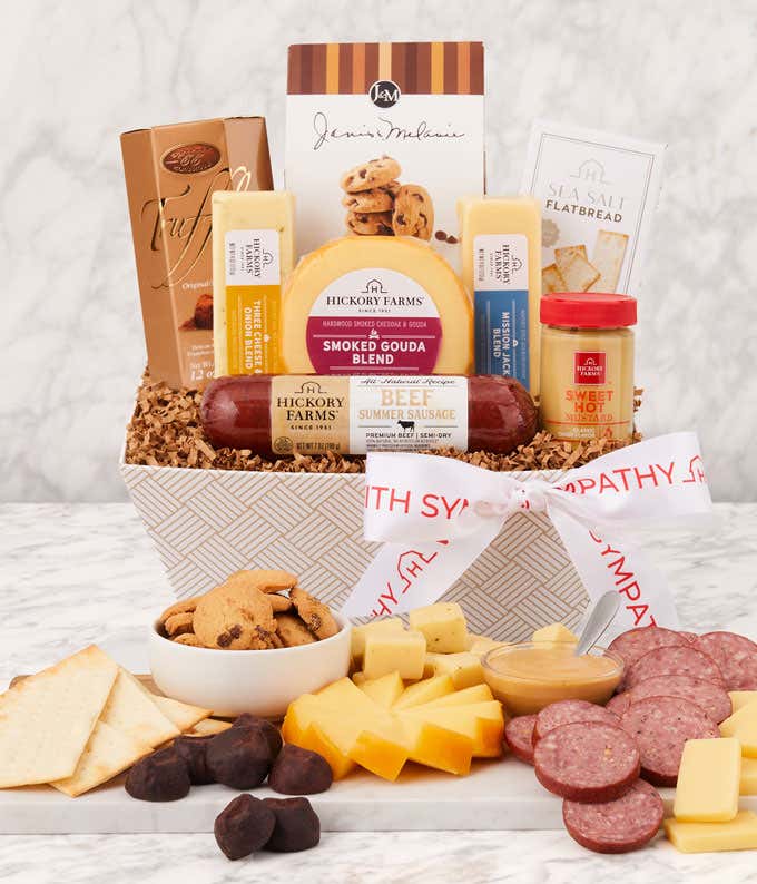 Sympathy gift basket with beef summer sausage, smoked gouda and cheddar cheese, sweet hot mustard, sea salt flatbread, chocolate chip cookies, truffles, and a sympathy ribbon, displayed with a charcuterie-style spread of meats, cheeses, and treats.