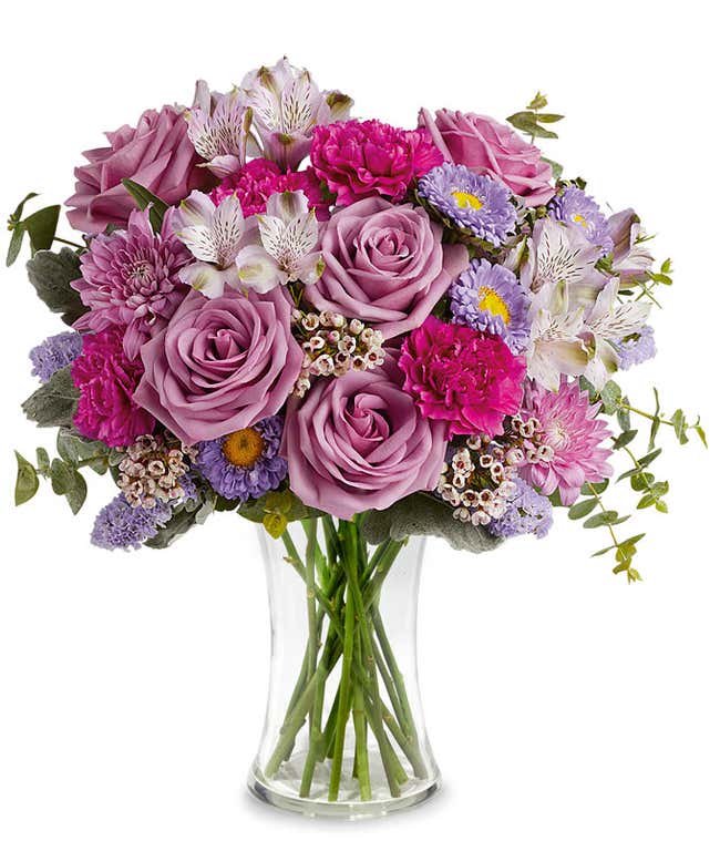 Image of a Mother's Day arrangement featuring Lavender Roses, Lavender Alstroemeria, Fuchsia Carnations, Lavender Matsumoto Asters, Lavender Cushion Spray Chrysanthemums, Lavender Sinuata Statice, Pink Waxflower, floral greens, all beautifully presented i