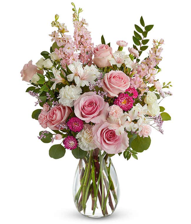 Image of a Mother's Day arrangement featuring Pink Roses, White Spray Roses, White Carnations, Ivory Alstroemeria, Miniature Pink Carnations, Pink Larkspur, Hot Pink Matsumoto Asters, and floral greens, all beautifully presented in a keepsake Pearl Pink S