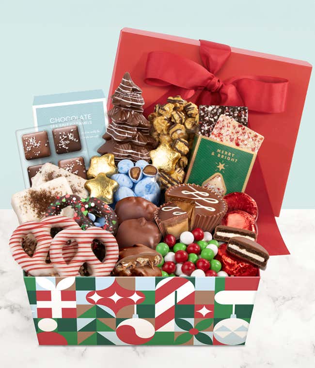 Festive gift box filled with assorted holiday treats, including chocolate-covered pretzels, popcorn, chocolate bark, cookies, colorful candy-coated chocolates, and holiday-themed chocolate bars, decorated with a red ribbon.