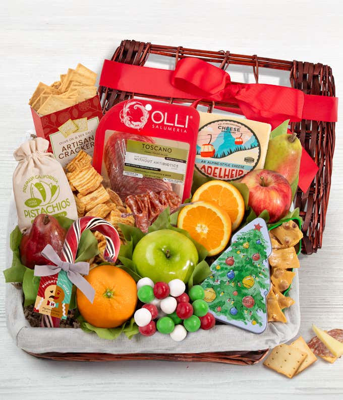 A wicker basket with artisan crackers, gourmet salami and cheese, peanut brittle, mustard, pistachios, fresh fruits like apples, pears, oranges, and an ornament-shaped cookie. A seasonal red bow completes the look, perfect for holiday gifting.