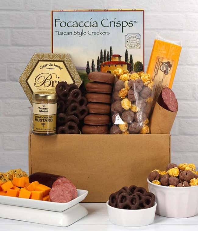 A gift box including focaccia crisps, two cheeses, mustard, brie cheese, summer sausage, chocolate-covered pretzels in a bowl, caramel popcorn, and six chocolate-covered Oreos for a sweet and savory gourmet experience.