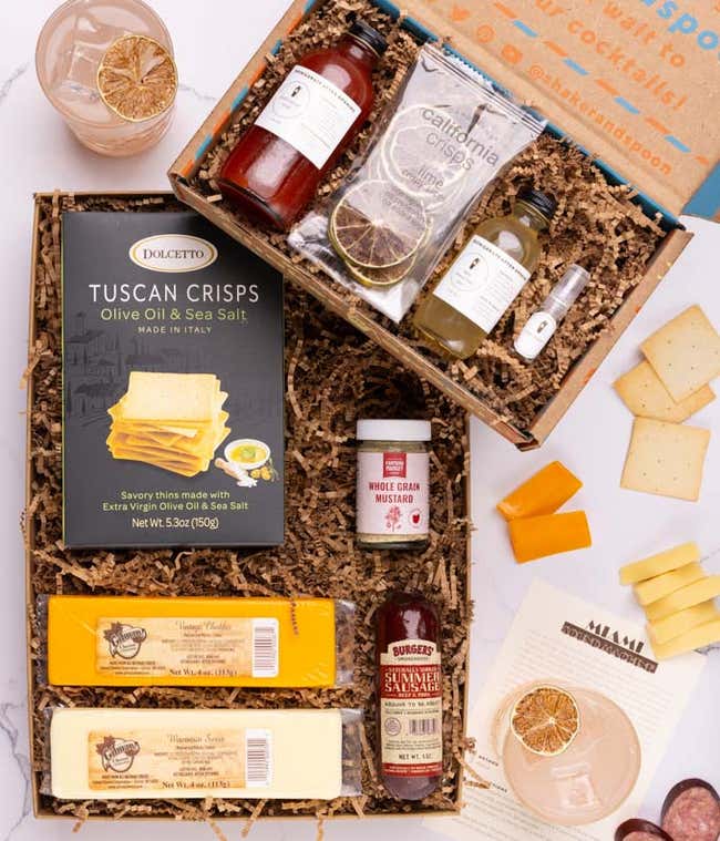 The food box contains two blocks of cheese, summer sausage, crackers and mustard.  The cocktail box contains tropical pink syrup, lemon-lime juice, rose water, dehydrated lime slices, and recipe card.