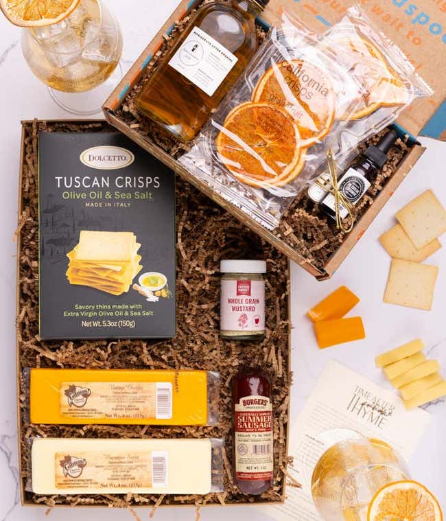The food box contains two blocks of cheese, summer sausage, crackers and mustard.  The cocktail box contains thyme-cucumber syrup, celery bitters, grapefruit oil mist, dehydrated grapefruit slices, and recipe card.