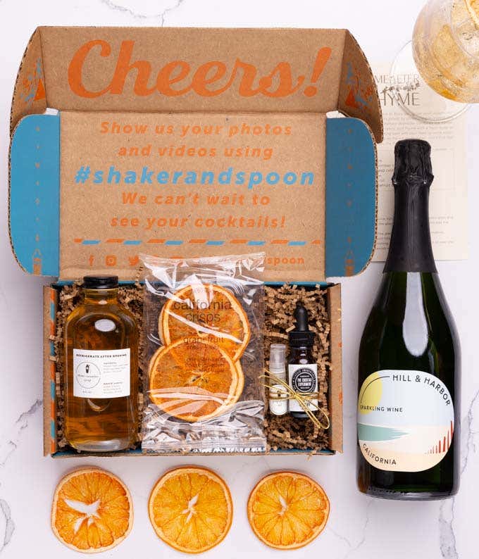 A bottle of Hill & Harbor Sparkling Wine alongside a cocktail kit box containing thyme-cucumber syrup, celery bitters, grapefruit oil finishing mist, dehydrated grapefruit slices and a recipe card.