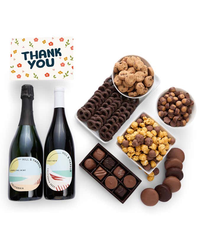 A gift box overflowing with treats including an assortment of chocolate-covered items like oreoes, almonds graham crackers and pretzels along with red velvet cookies, hazelnut wafers, an 8 piece box of chocolates, 2 bottles of wine and a Thank You card.