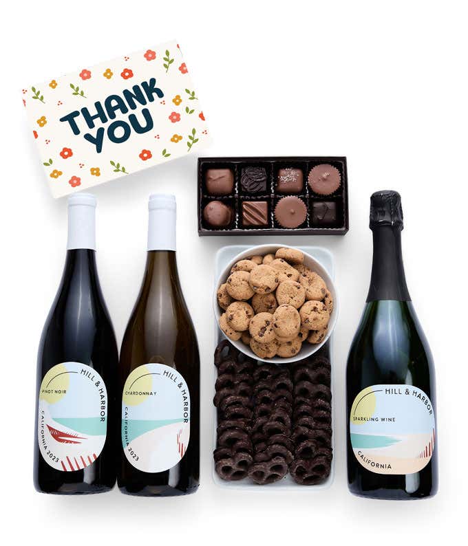 A gift box with chocolate pretzels, chocolate graham crackers, red velvet cookies, hazelnut wafer rolls, an 8 piece box of chocolates, 3 bottles of wine and a Thank You message card.